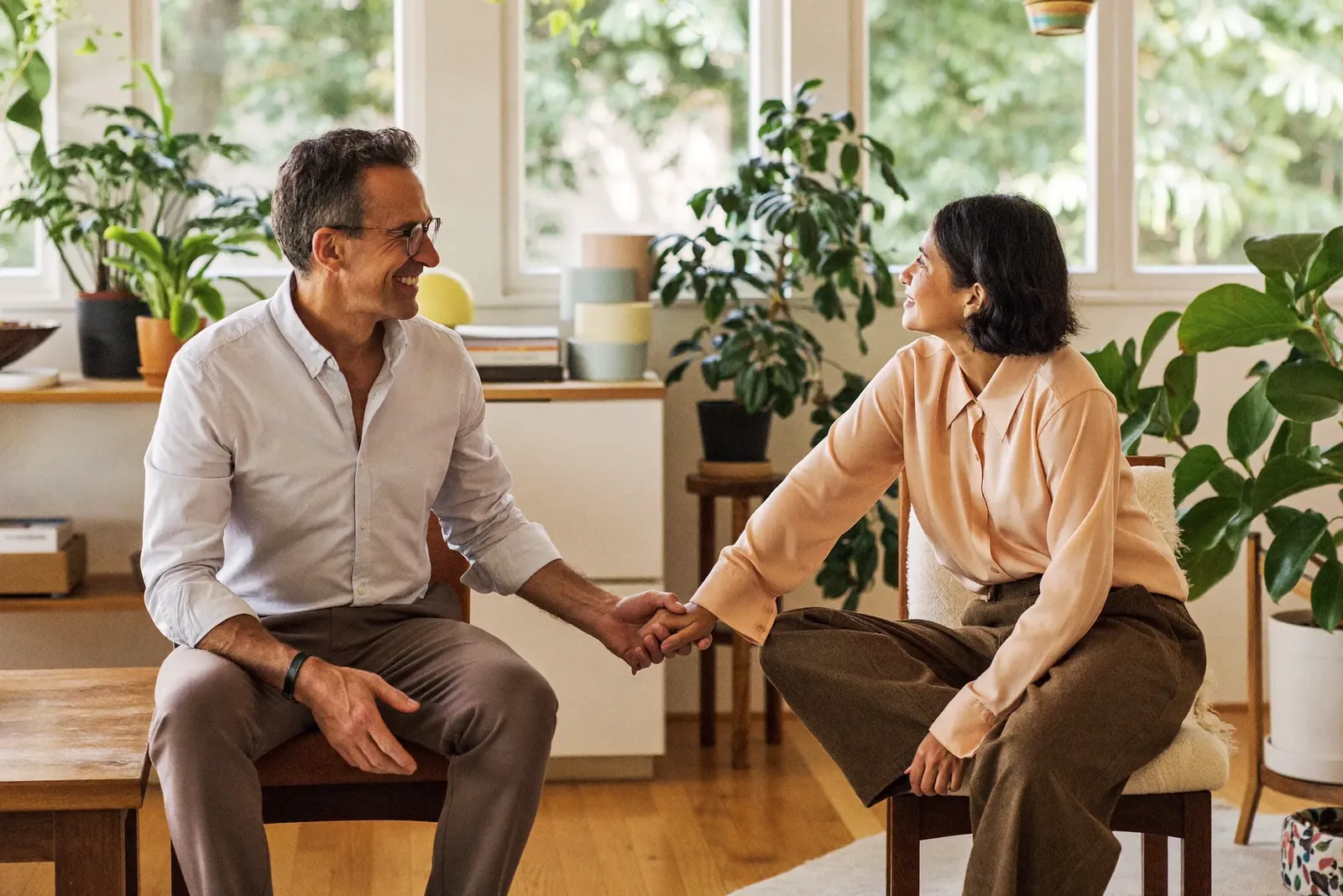 A couple sitting on chairs facing each other, reaching to hold hands