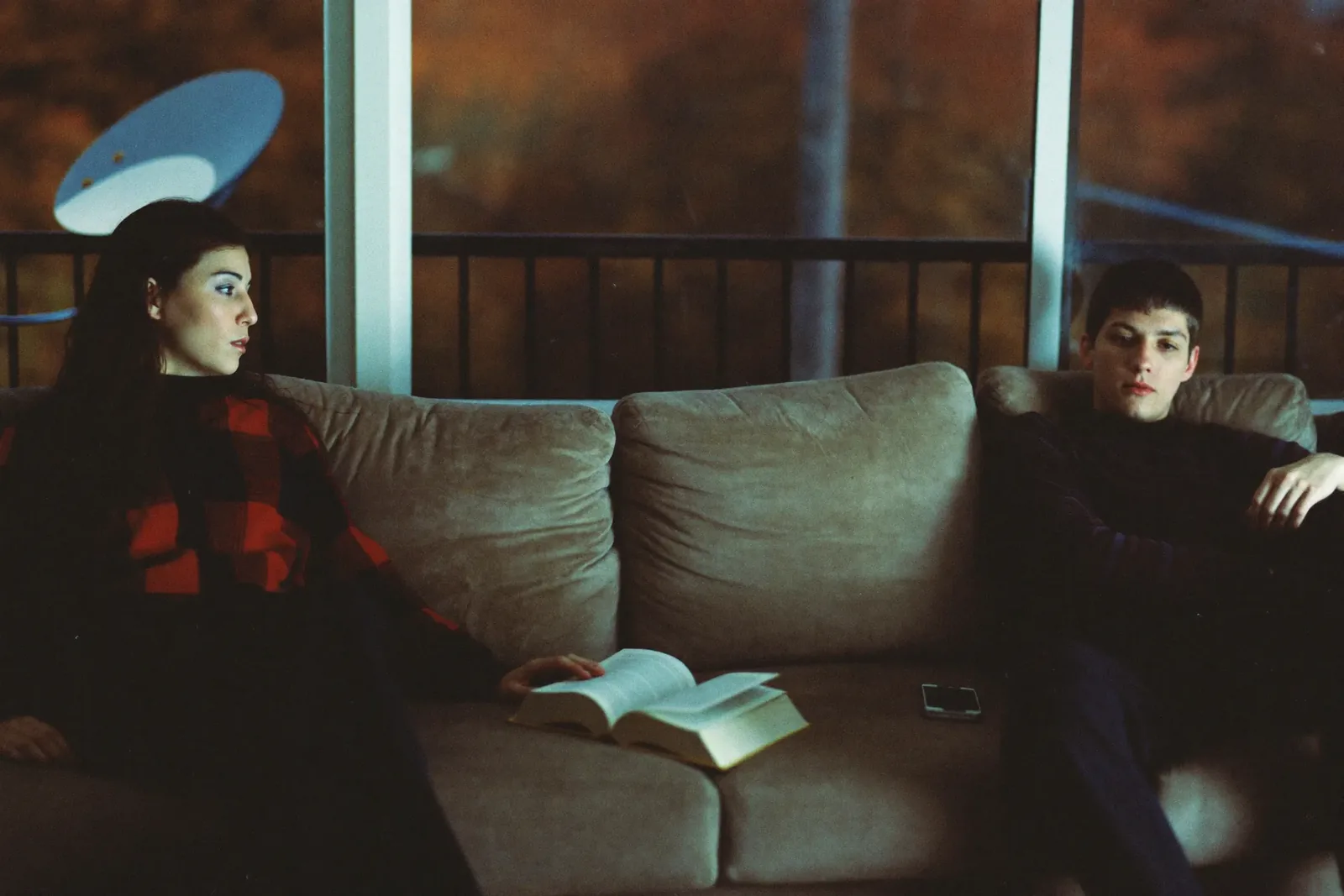 Two partners at opposite ends of a sofa in the evening, a book and a phone between them