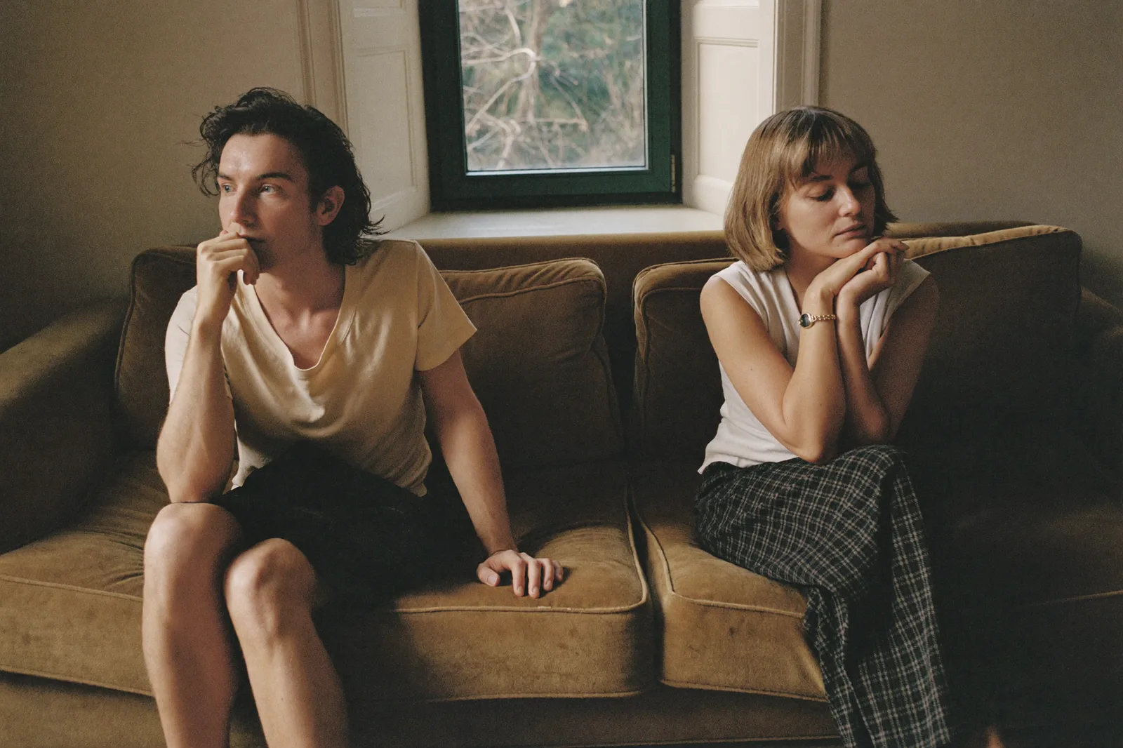 A couple on a mustard sofa, sitting close but each turned toward a different corner of the room