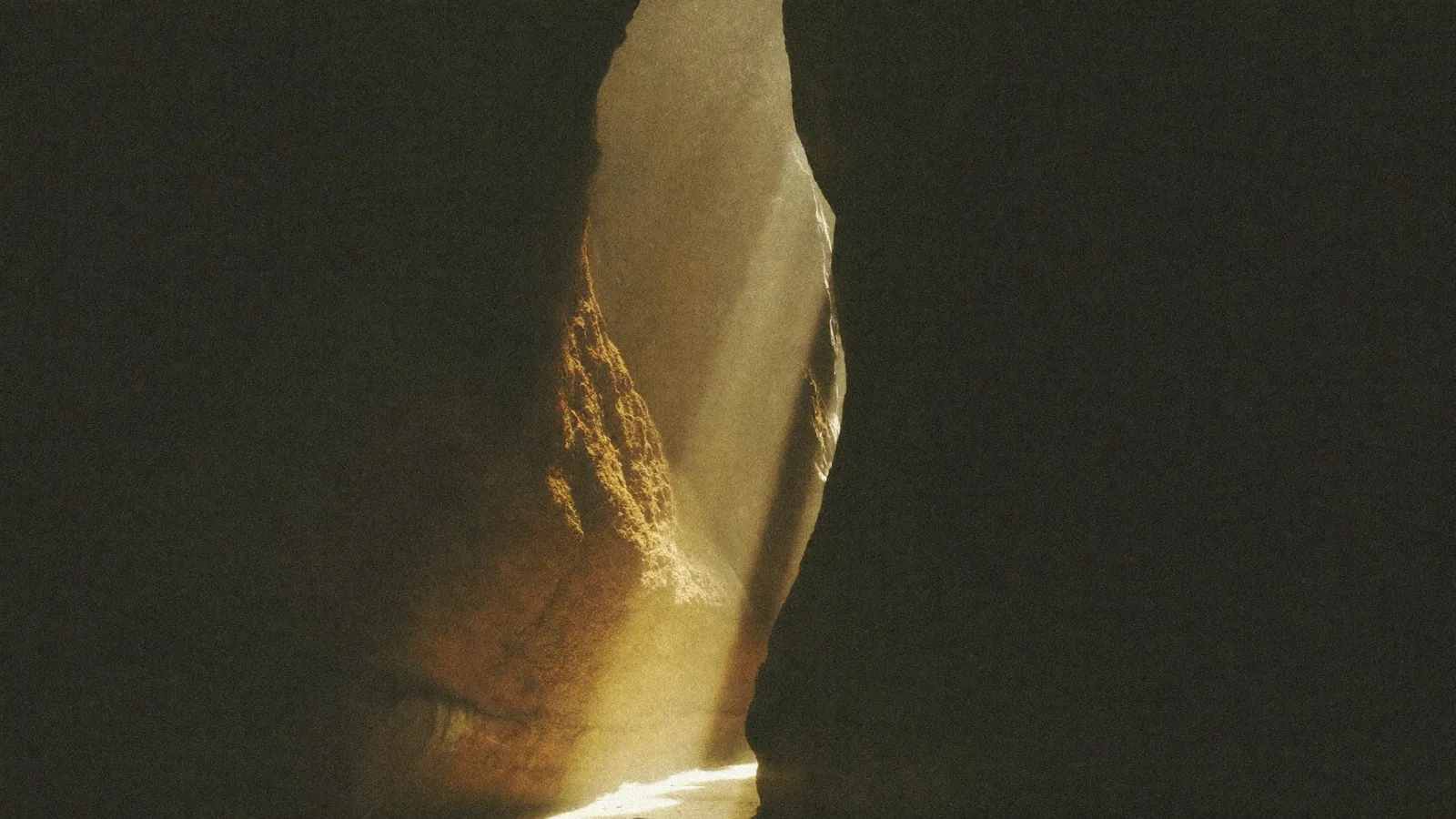 A narrow dark canyon with one warm beam of light reaching the ground