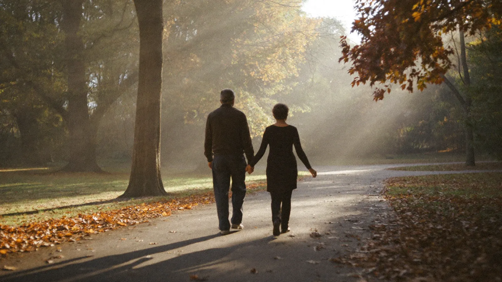 A couple walking together down an autumn path toward the light